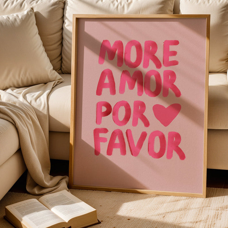 Framed artwork with 'More Amor Por Favor' text on a pink background, placed on a beige couch.
