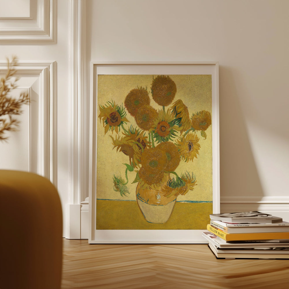Framed artwork of sunflowers on a wall in a room with books and a chair.